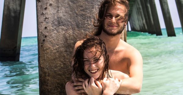 Young, happy couple at the beach. He stands behind her with arms around her shoulders