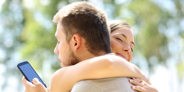 Couple embracing and male of the couple is texting over her shoulder